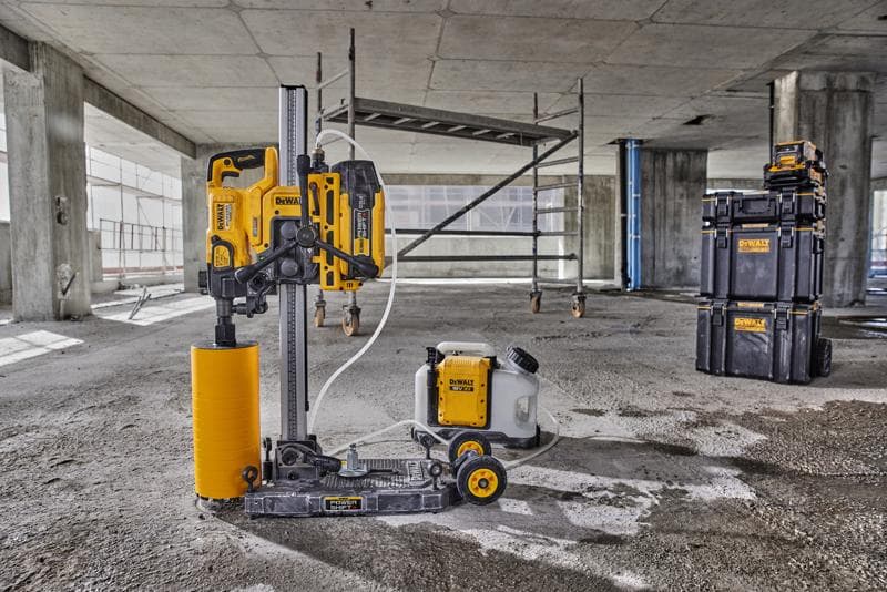Uma máquina de perfuração de núcleo DEWALT com broca cilíndrica amarela, tanque de água e caixas de armazenamento pretas está montada em um piso de concreto em um canteiro de obras.