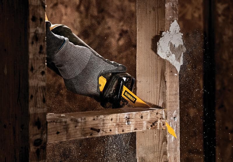 Uma mão com luva usando uma lâmina de serra recíproca DEWALT para cortar uma estrutura de madeira, com serragem e detritos voando ao redor.