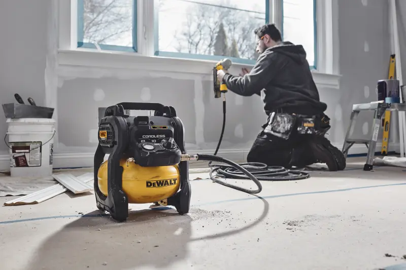 Compressor sem fio DEWALT em sala reformada, trabalhador usa pistola de pregos na janela.
