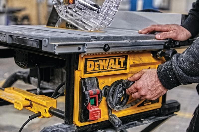 Close-up de uma pessoa ajustando as configurações em uma serra de mesa DEWALT, com painel de controle amarelo com botões e mostradores em um ambiente de oficina.
