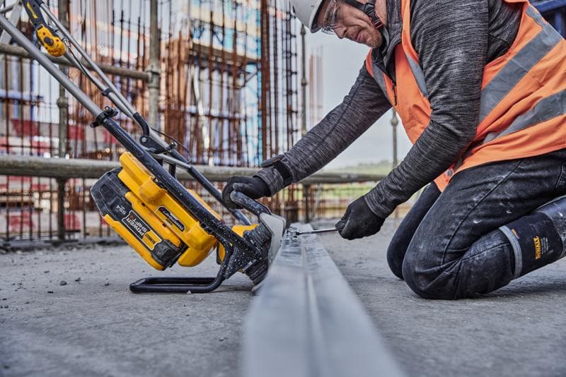 Uma pessoa com equipamento de segurança de construção usa uma ferramenta elétrica sem fio DEWALT (SKU: DCPS330N) em uma viga de metal em um canteiro de obras.