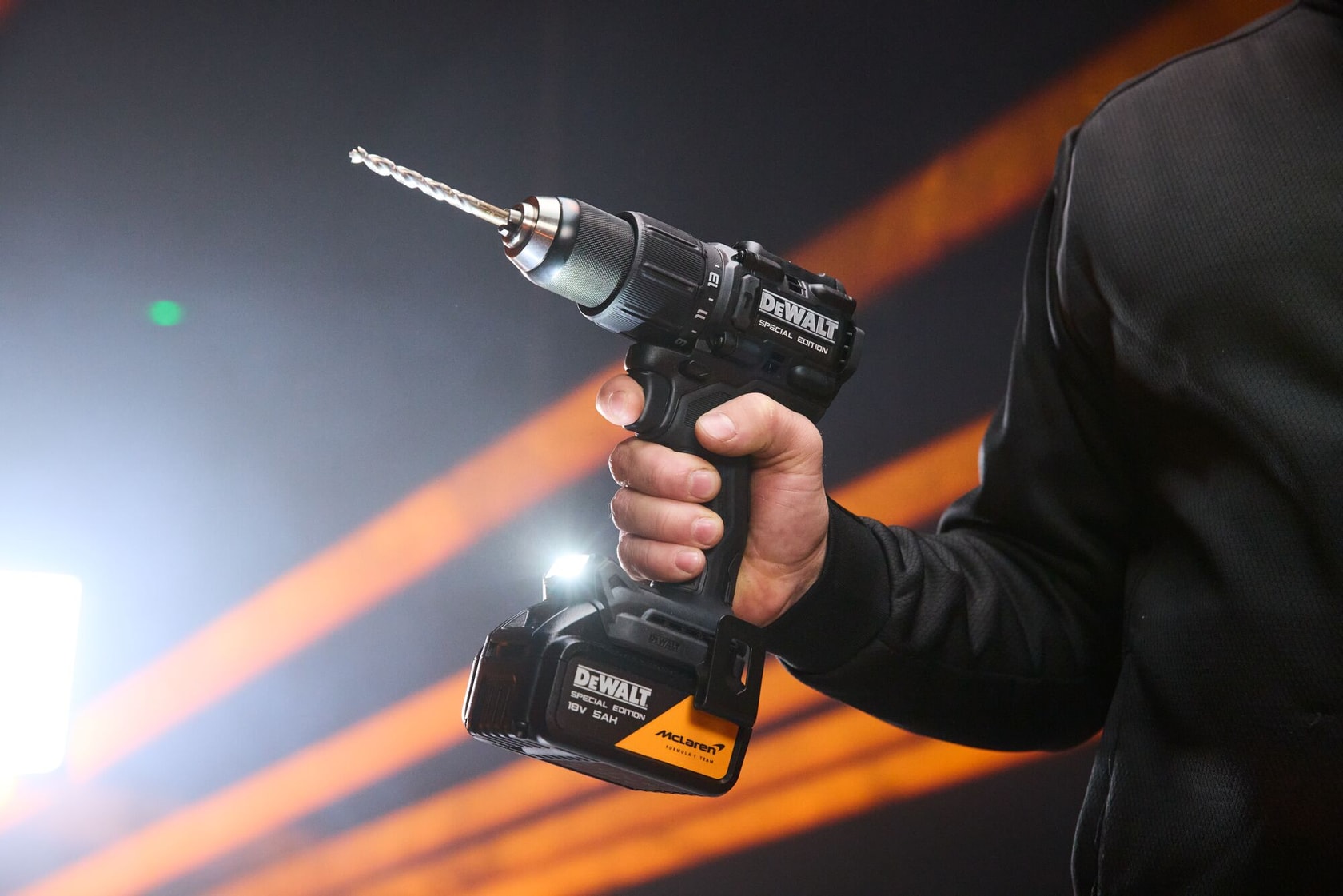 A hand holds the DEWALT x McLaren F1 Team 18V XR Special Edition Hammer Drill Driver with 5Ah battery