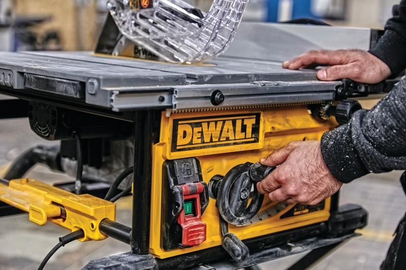 Close-up de uma pessoa ajustando as configurações em uma serra de mesa DEWALT, com painel de controle amarelo com botões e mostradores em um ambiente de oficina.